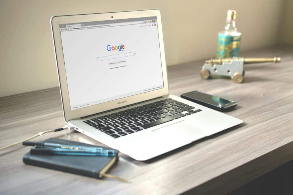 A MacBook displaying Google search on a desk with a notebook, pen, phone, and decorative items. | Tsunami Reach