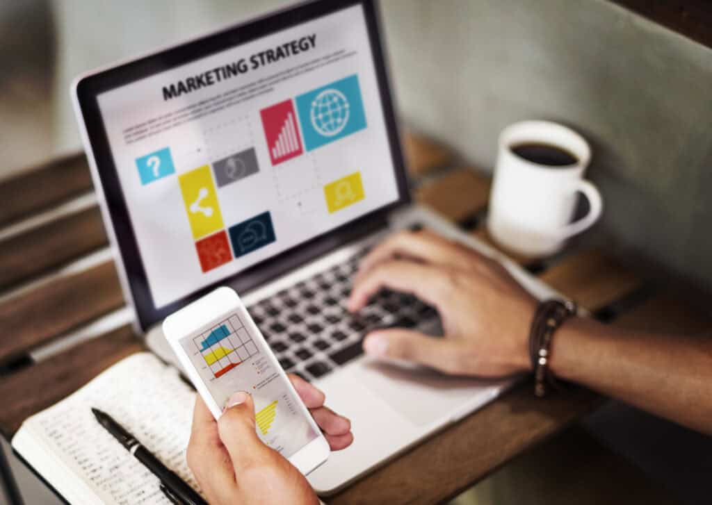 Person working on a laptop with a marketing strategy on the screen and holding a smartphone with a graph. | Tsunami Reach