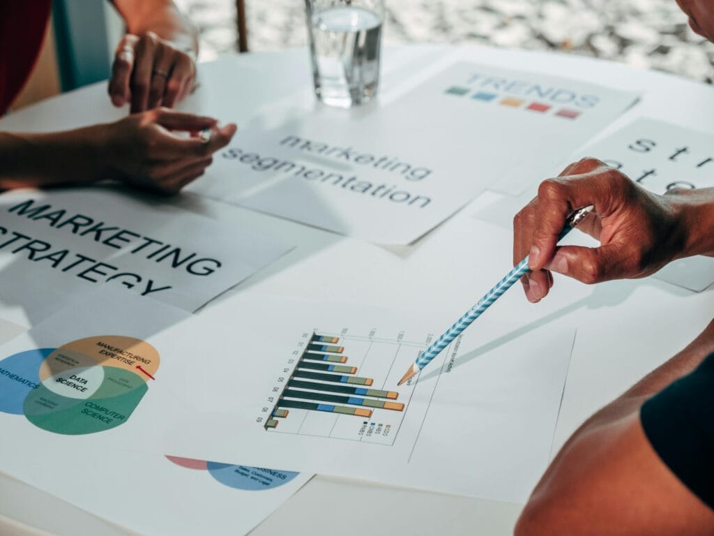 People discussing marketing strategy, segmentation charts, and bar graphs at a table with documents and a glass of water. | Tsunami Reach