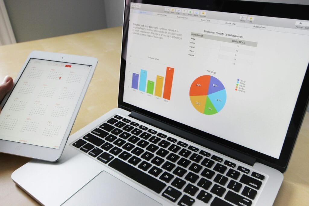 A person holds a tablet with a calendar next to a laptop displaying charts and graphs on a desk. | Tsunami Reach