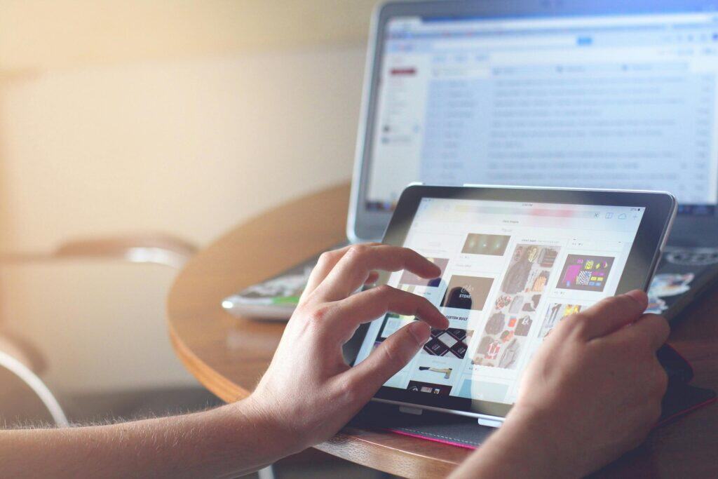 Person browsing images on a tablet with a laptop displaying an email inbox in the background on a table. | Tsunami Reach