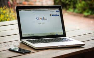 A MacBook Pro on a wooden table displays the Google homepage, with a smartphone beside it. | Tsunami Reach