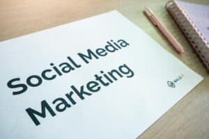 A sheet of paper with "Social Media Marketing" printed on it, beside a pen and a spiral notebook on a desk. | Tsunami Reach