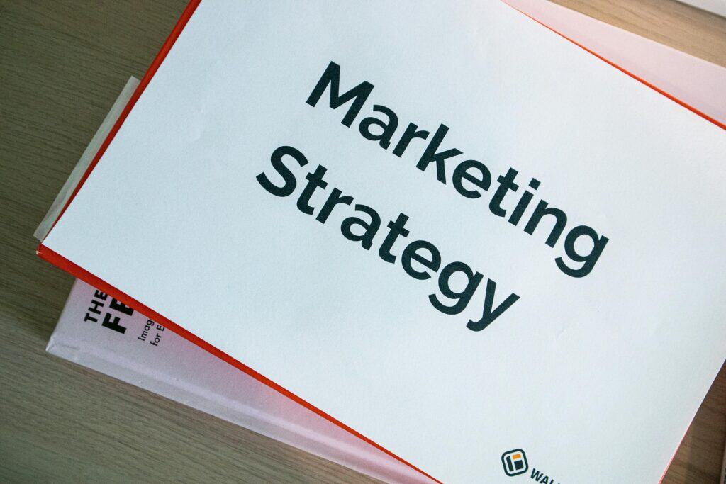 A paper titled "Marketing Strategy" placed on top of a stack of books on a wooden table. | Tsunami Reach