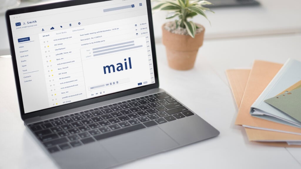 A laptop on a desk displays an email inbox, with folders and messages visible. A plant and folders are nearby. | Tsunami Reach