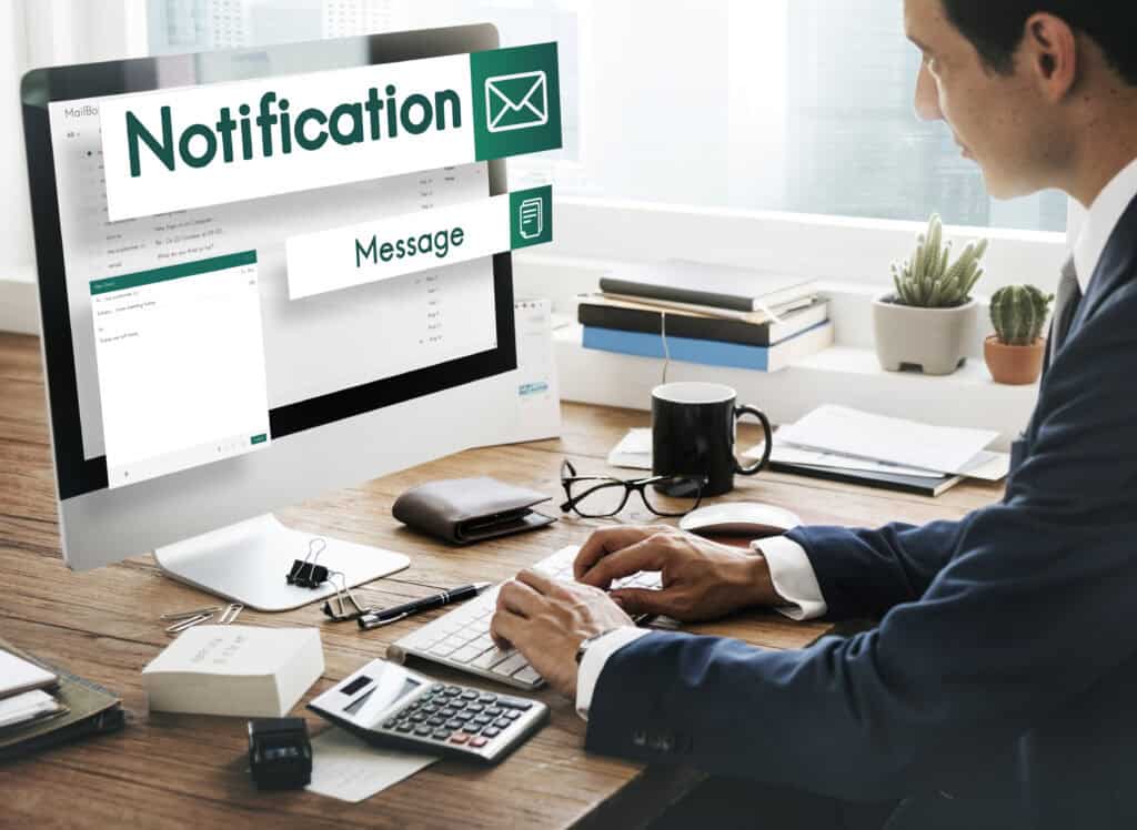 A man in a suit works at a desk with a computer, receiving email and message notifications on the screen. | Tsunami Reach