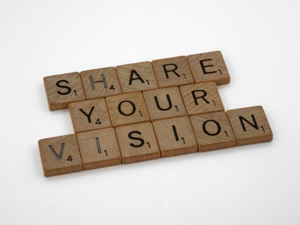 Wooden Scrabble tiles arranged to spell "SHARE YOUR VISION" on a white background. | Tsunami Reach