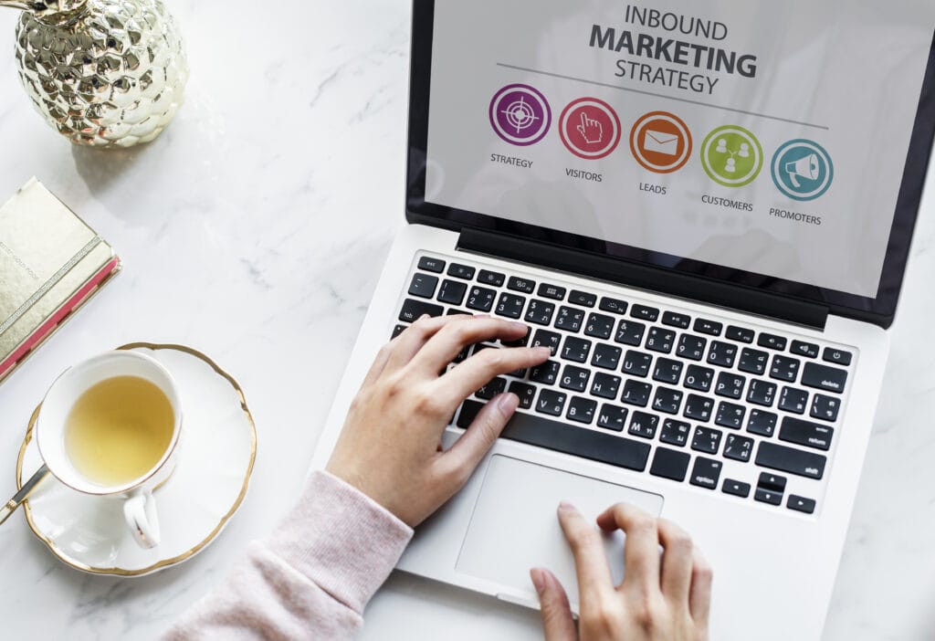 Person typing on a laptop displaying an inbound marketing strategy diagram, next to a cup of coffee on a white desk. | Tsunami Reach