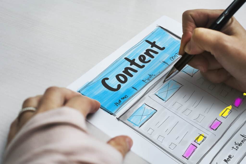 A person sketches a colorful website layout labeled “Content” with sections and navigation links on paper. | Tsunami Reach