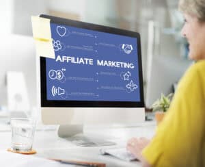 Person working at a desk with a computer screen displaying an affiliate marketing diagram and related icons. | Tsunami Reach