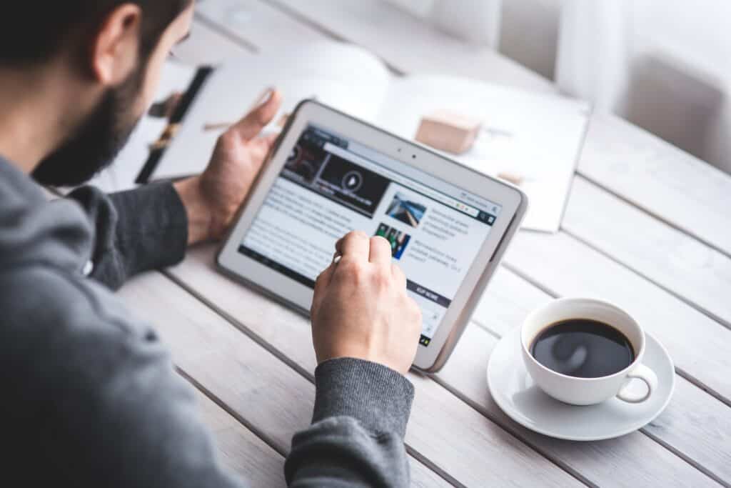 A person uses a tablet at a table with a cup of coffee and an open magazine nearby. | Tsunami Reach
