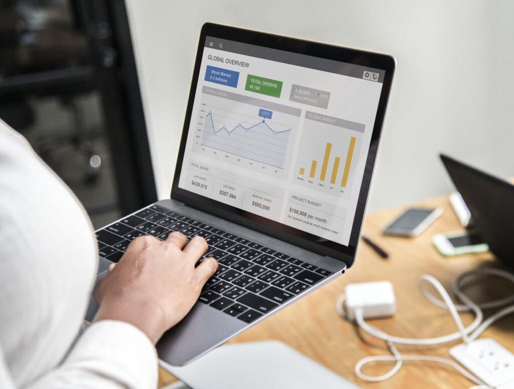 Person using a laptop displaying graphs, charts, and financial data on a dashboard at a desk. | Tsunami Reach
