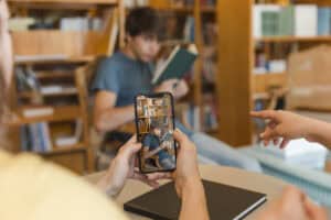 Person takes a photo of a young man reading a book in a library, with bookshelves in the background. | Tsunami Reach