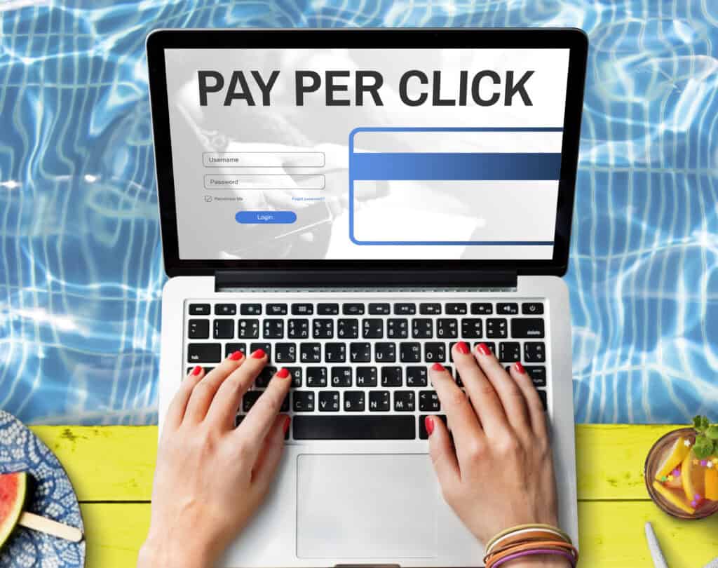 Hands on a laptop showing a "Pay Per Click" login screen, with a pool and fruit in the background. | Tsunami Reach