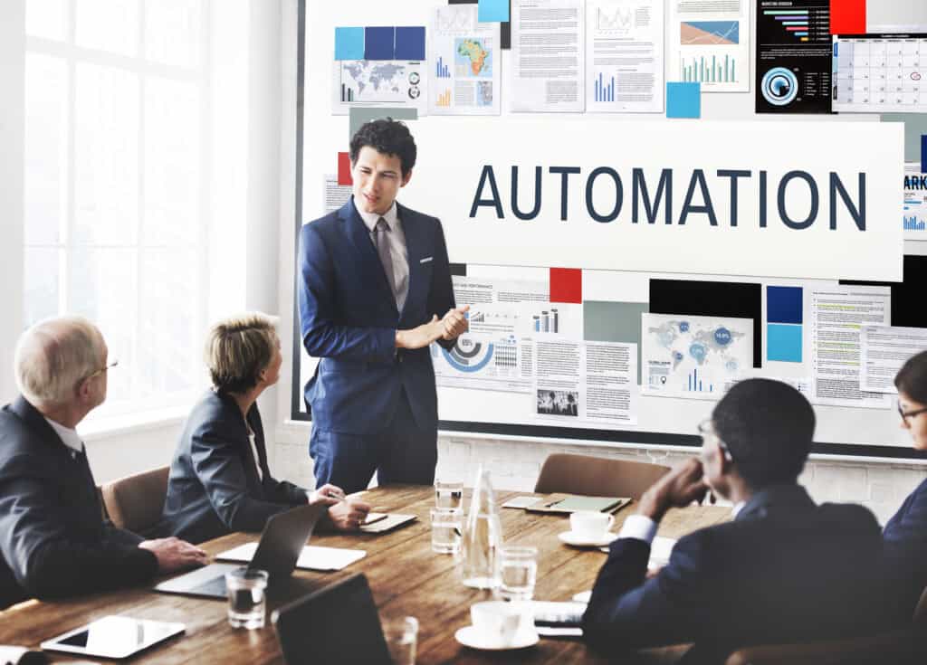 Businessman presenting about automation to colleagues in a conference room, with charts and data on the wall behind him. | Tsunami Reach