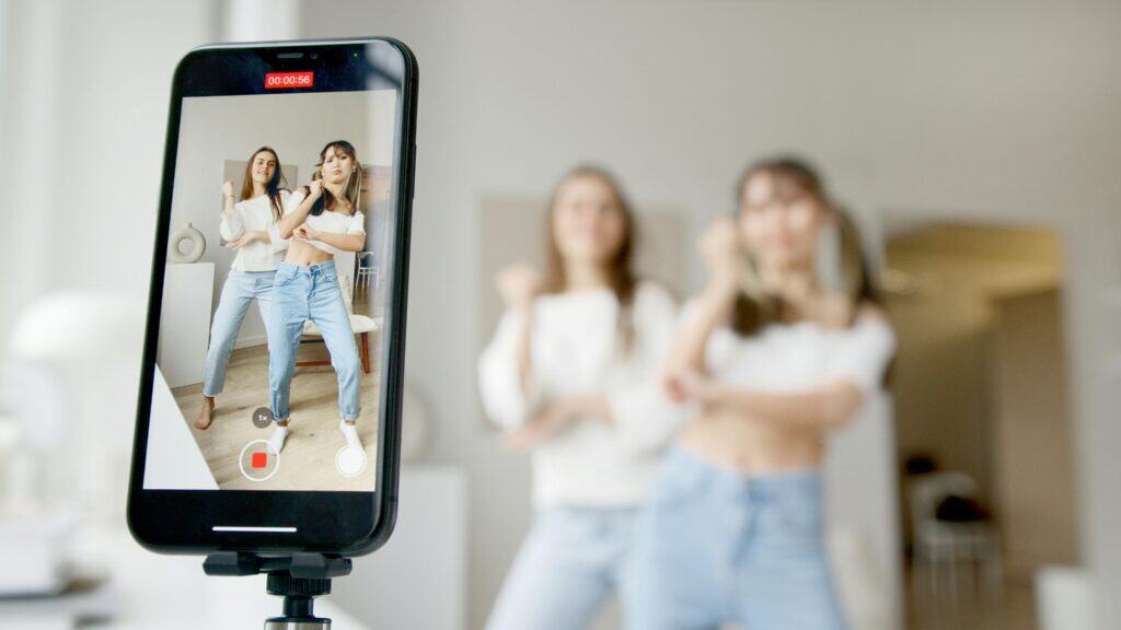 Two women dance in front of a smartphone on a tripod, recording a video in a bright, modern room. | Tsunami Reach