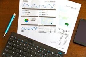 Paper with analytics charts and graphs on a desk, next to a blue pen, a keyboard, and a smartphone. | Tsunami Reach