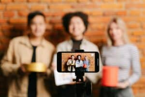 A smartphone on a tripod films three people posing and smiling against a brick wall background. | Tsunami Reach