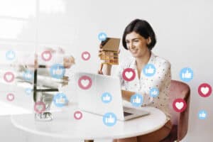 Woman recording a makeup tutorial at her laptop, surrounded by social media icons, showcases her content strategy. | Tsunami Reach