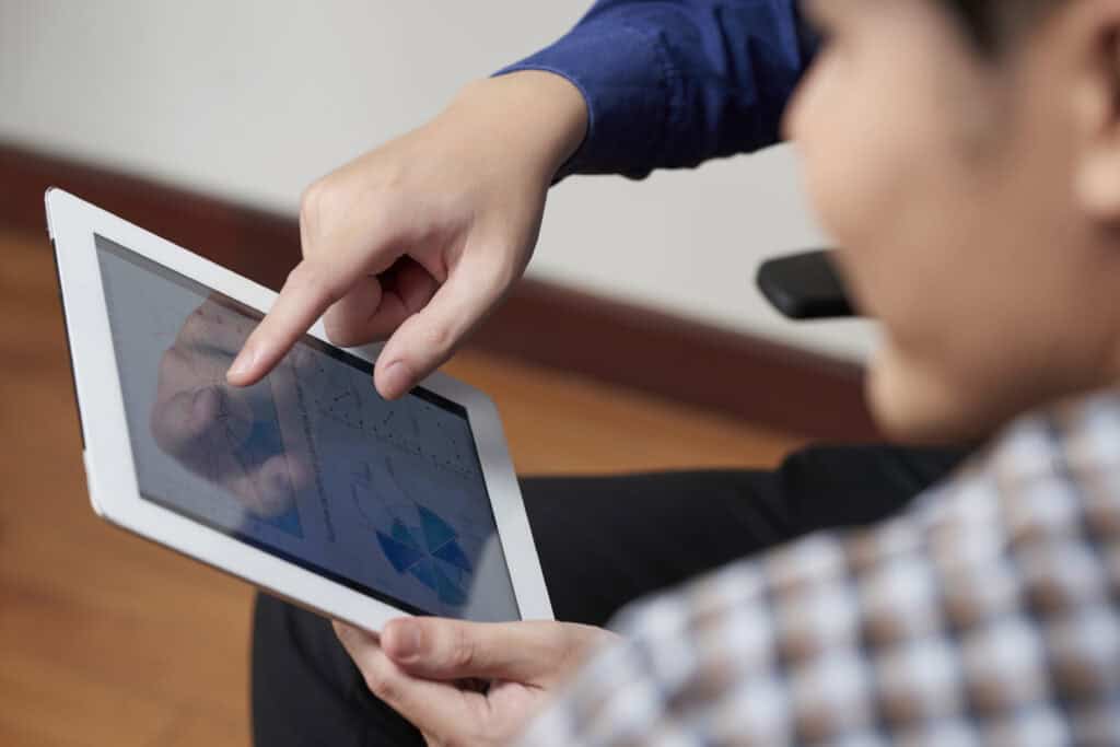 Person points at data charts on a tablet screen while another person looks on closely. | Tsunami Reach