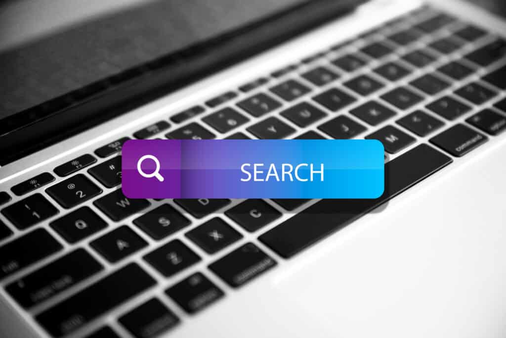 A search bar graphic over a laptop keyboard, with a magnifying glass icon and the word "SEARCH. | Tsunami Reach