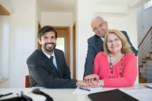 Smiling man in a suit sits at a desk with an older couple, all holding hands and looking at the camera. | Tsunami Reach