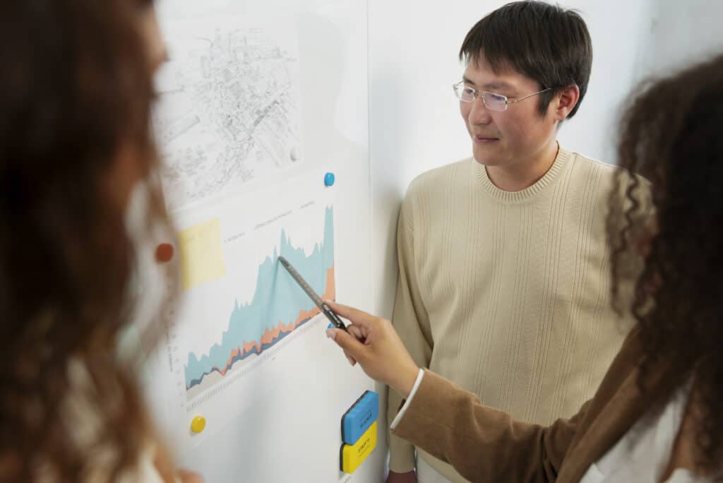 Two people discussing a graph on a whiteboard, with one person pointing at the chart using a pen. | Tsunami Reach