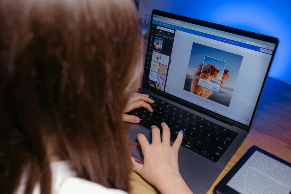 A person using a laptop to edit a lion image, with a tablet on the desk nearby. | Tsunami Reach