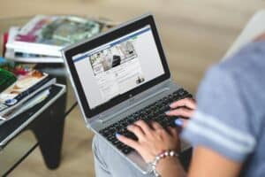 Person using a laptop with Facebook open, sitting at a glass table with magazines nearby. | Tsunami Reach