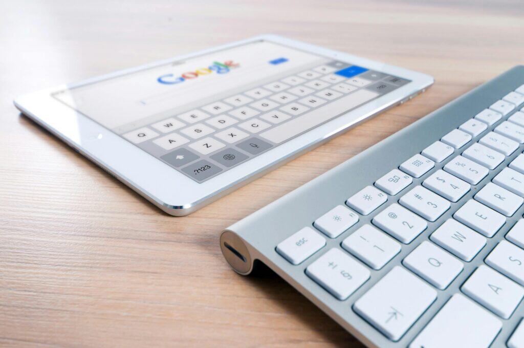 A tablet displaying a Google search page next to a wireless keyboard on a wooden desk. | Tsunami Reach