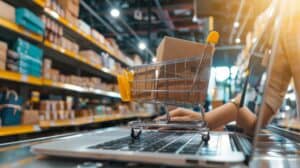 A small shopping cart with a box sits on a laptop keyboard in a warehouse with shelves of packages. | Tsunami Reach