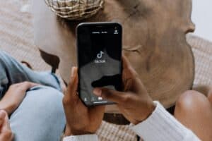 A person holds a smartphone displaying the TikTok app, with a wooden table in the background. | Tsunami Reach