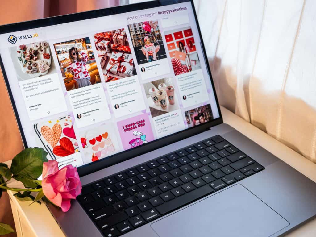 A laptop displays a Valentine's Day-themed social media feed; a pink rose rests on the keyboard. | Tsunami Reach