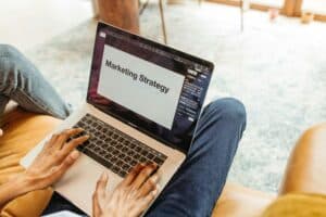 Person typing on a laptop displaying a presentation slide titled "Marketing Strategy. | Tsunami Reach