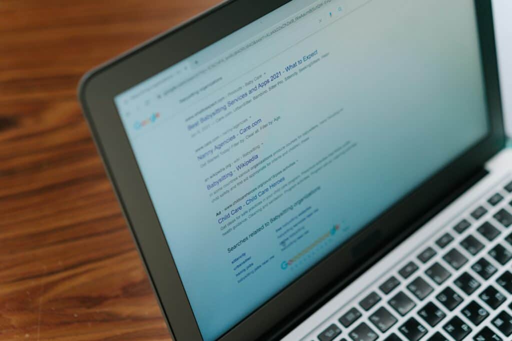 A laptop screen displays Google search results for "best babysitting services" on a wooden table. | Tsunami Reach