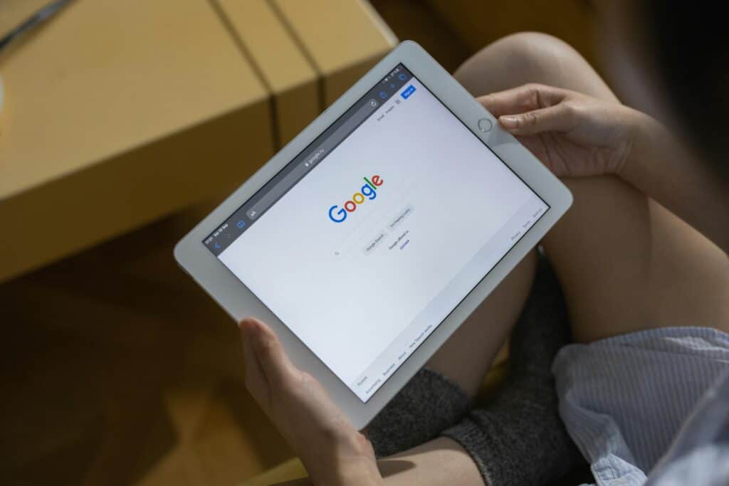 Person holding a tablet with the Google search homepage open on the screen, sitting indoors. | Tsunami Reach