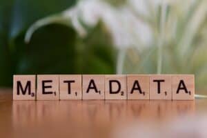 Wooden Scrabble tiles spell out the word "METADATA" on a table, with a blurred green and white background. | Tsunami Reach