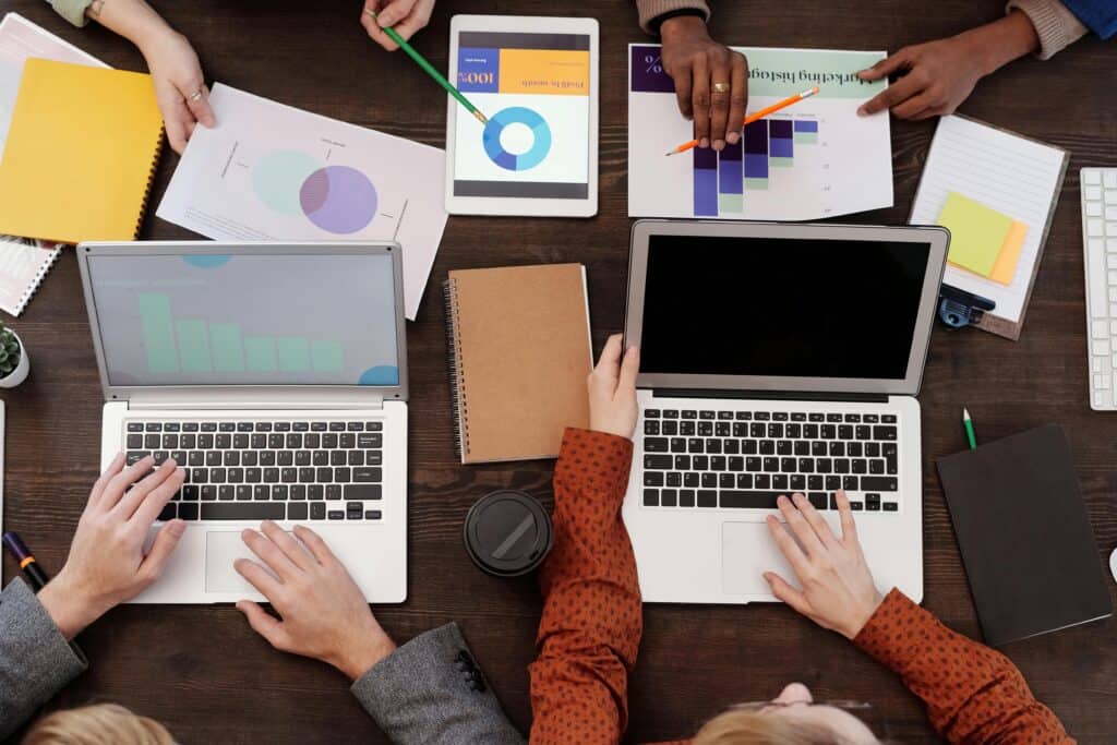 People working at a table with laptops, notebooks, charts, and graphs, collaborating on a project. | Tsunami Reach