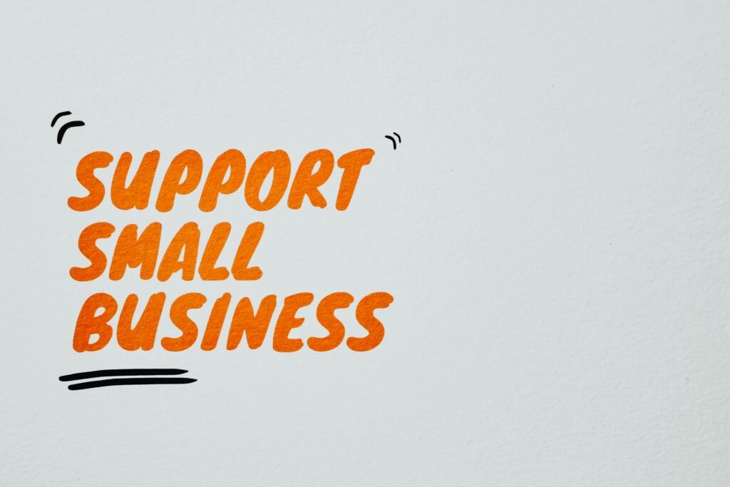 Text "Support Small Business" in bold orange letters on a plain white background with decorative black lines. | Tsunami Reach