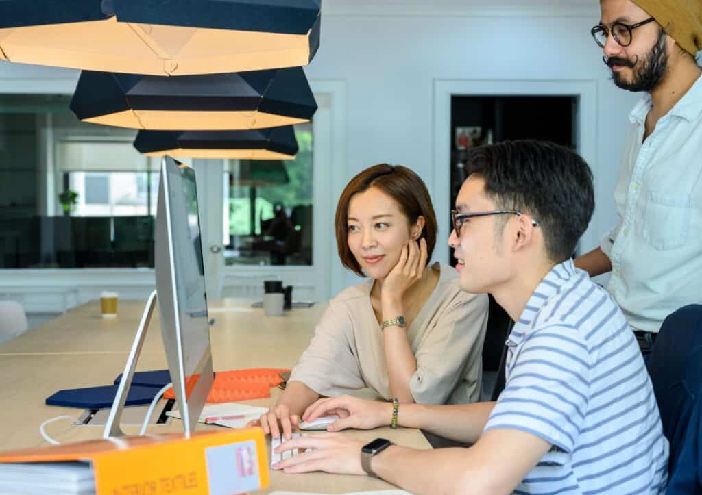 Three people collaborating at a desk in a modern digital marketing agency, focused on a computer monitor. | Tsunami Reach