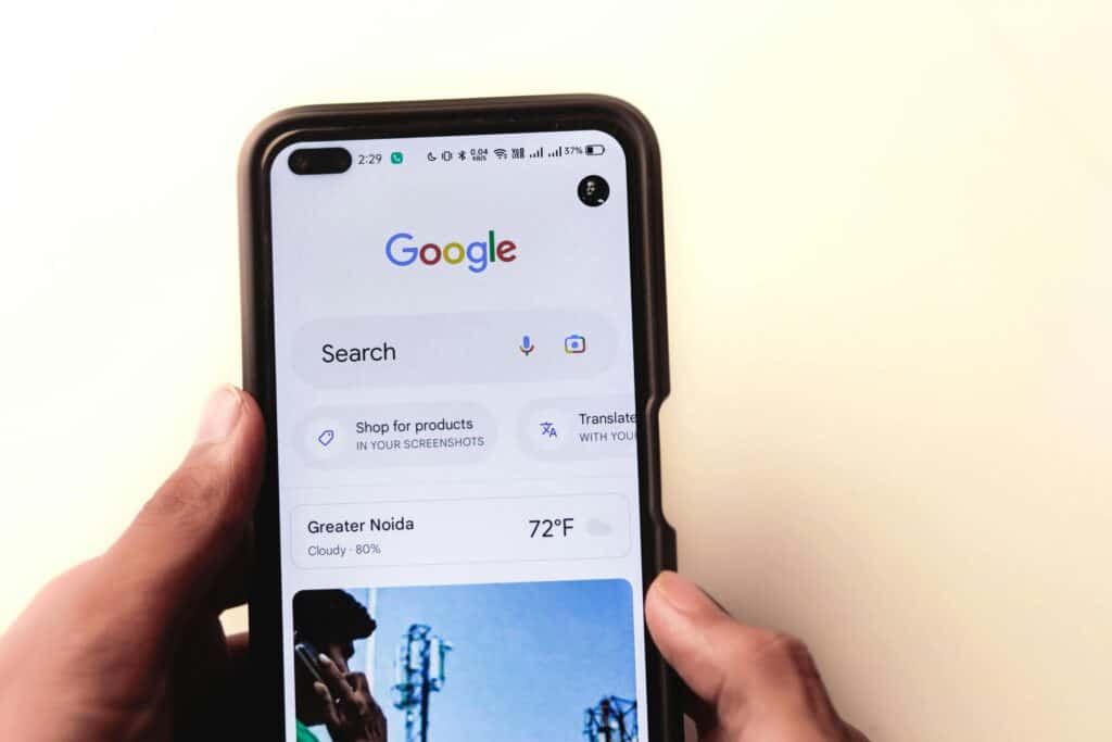 Person holding a smartphone displaying the Google search homepage with weather and suggestions visible. | Tsunami Reach