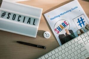 A desk with a lightbox reading "#SOCIAL," Hashtag Marketing Guide, pen, keyboard, and social media button. | Tsunami Reach
