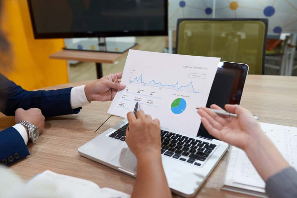 Two people discuss a printed chart with graphs and data while sitting at a desk with a laptop. | Tsunami Reach