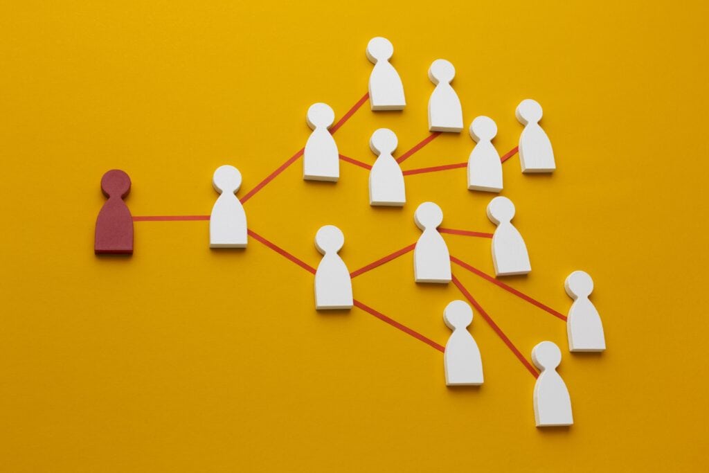 Flat lay of a red figure connected by red lines to multiple white figures on a yellow background, illustrating networking. | Tsunami Reach