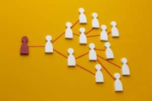 Flat lay of a red figure connected by red lines to multiple white figures on a yellow background, illustrating networking. | Tsunami Reach