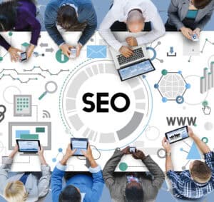 People using digital devices around a table with "SEO" and web-related graphics, symbolizing an SEO agency Singapore. | Tsunami Reach