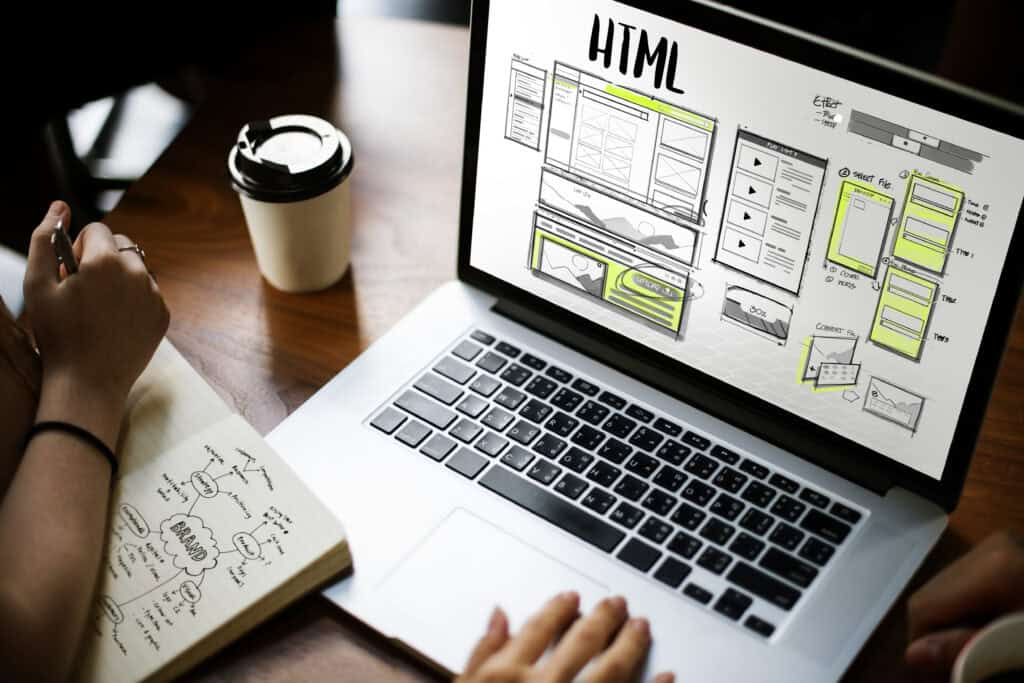Two people work at a desk; one sketches notes while the other reviews an SEO content marketing website mockup on a laptop. | Tsunami Reach