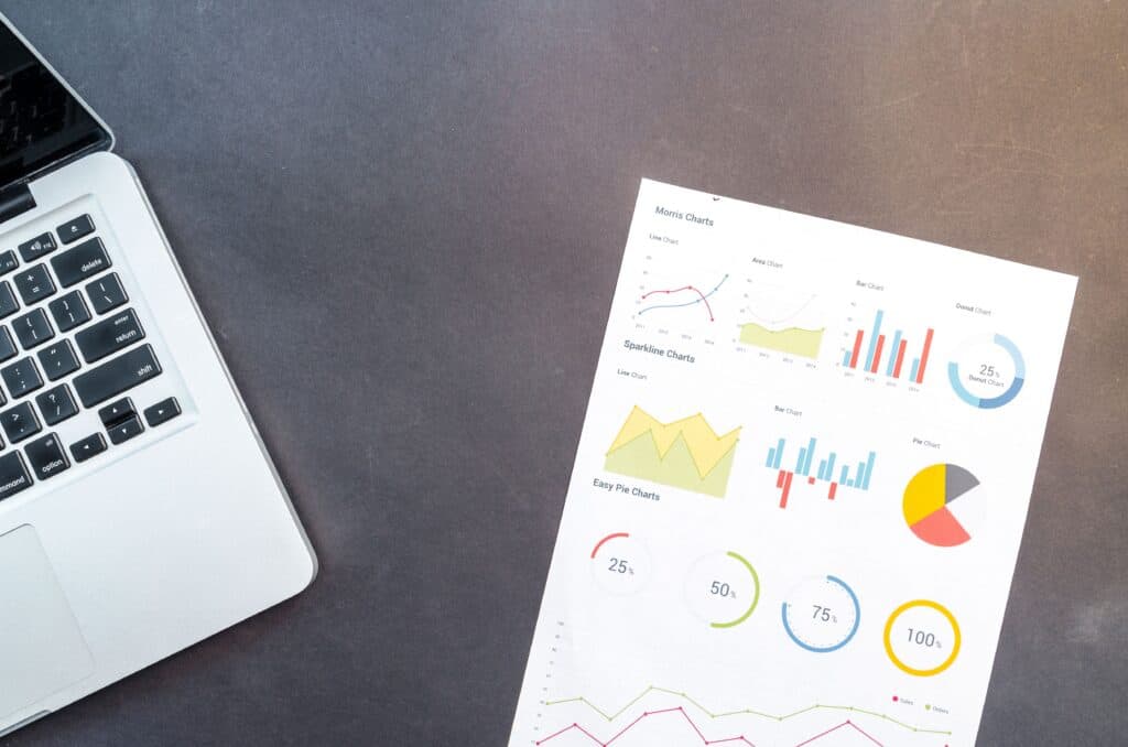 Paper with colorful charts and graphs next to a laptop on a dark desk. | Tsunami Reach