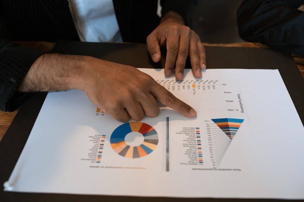 A person points at a printed chart with graphs, analyzing business or financial data on a desk. | Tsunami Reach