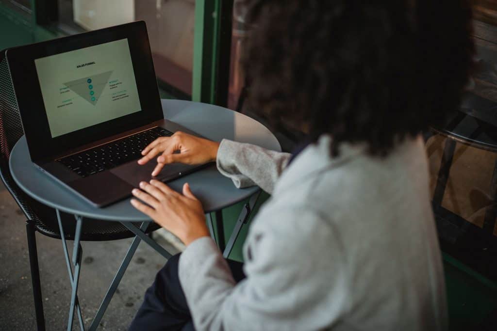 Person using a laptop at a small round table, viewing a presentation slide with a funnel diagram. | Tsunami Reach